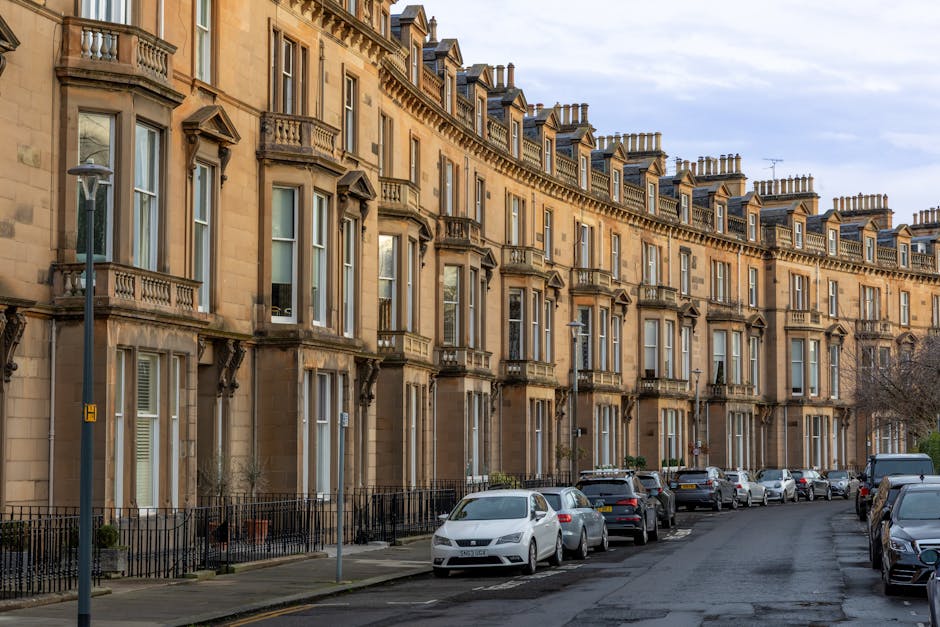 A row of Victorian terraced houses on Stroud Green Road in Finsbury Park, featuring brick facades with white bay window frames and decorative cornices. The houses have small front gardens enclosed by black iron fences, with some greenery such as bushes and small trees. The street is lined with parked cars along the curb, and the roadway is clean and well-maintained under soft natural lighting, typical of an early evening setting. The scene reflects a typical residential area in Finsbury Park with attention to surface cleanliness and structural maintenance, emblematic of the type of properties serviced by Finsbury Park Carpet Cleaners with professional surface cleaning and deep cleaning solutions.